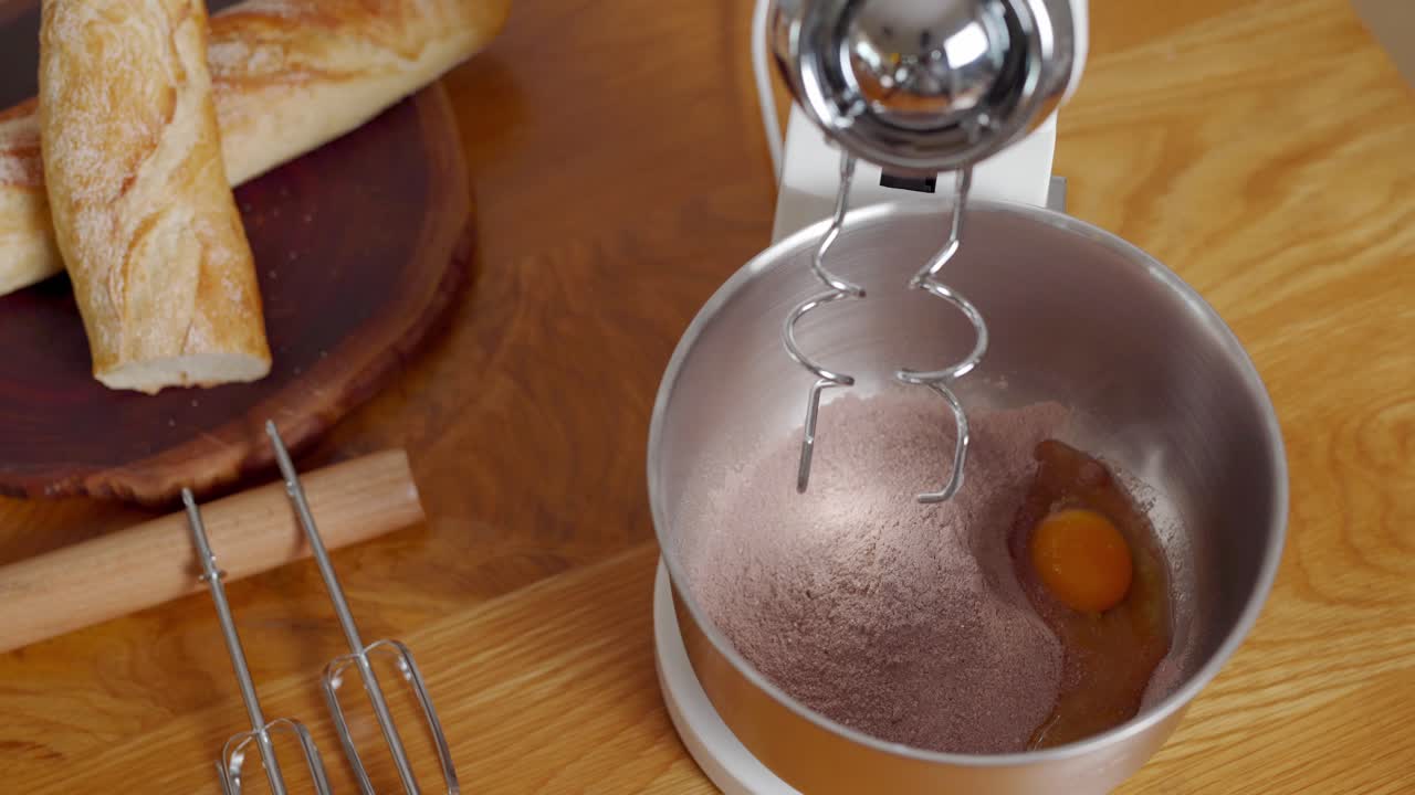 Hands putting ingredients for delicious cake in bowl, stand mixer whisking batter