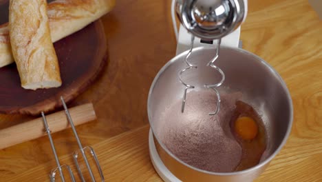 hands putting ingredients for delicious cake in bowl, stand mixer whisking batter