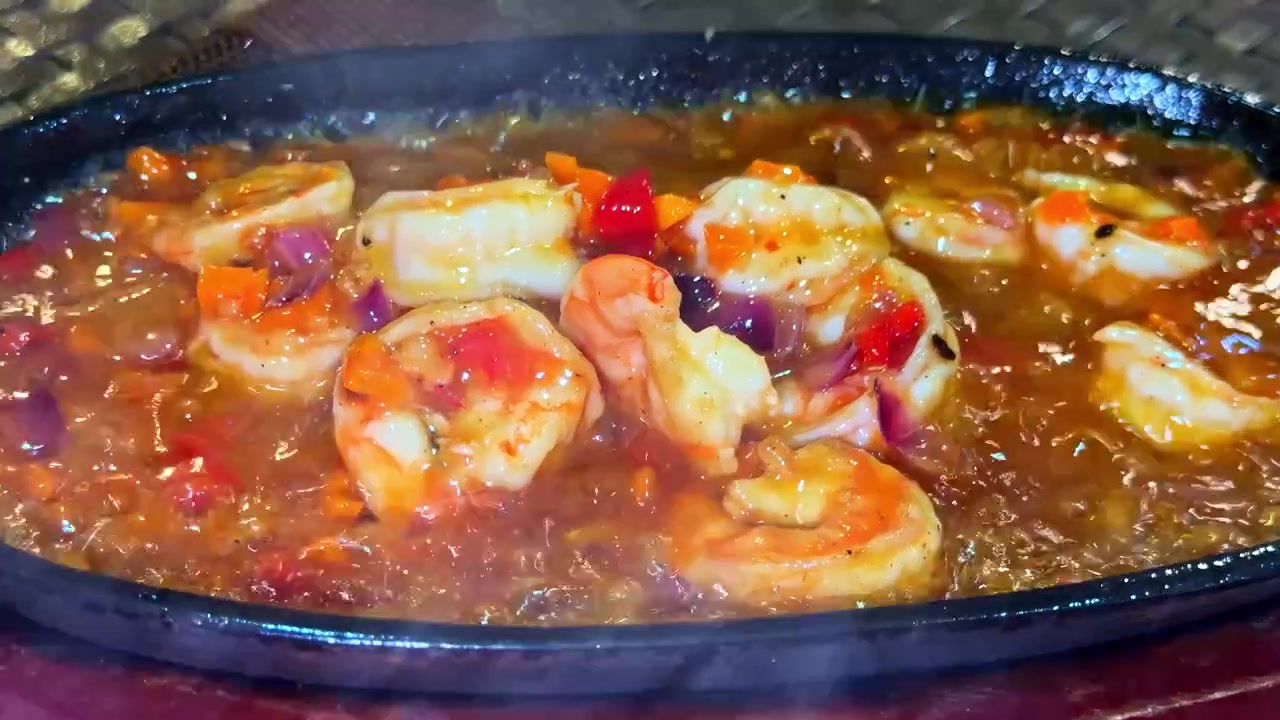 Primo piano di una padella con gamberoni che friggono nell'olio con verdure.