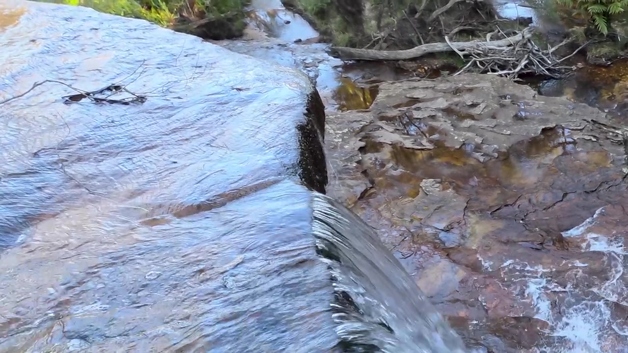 Primo piano di acqua che scorre su un bordo di scogliera di arenaria nel Parco Nazionale delle Blue Mountains, Australia.