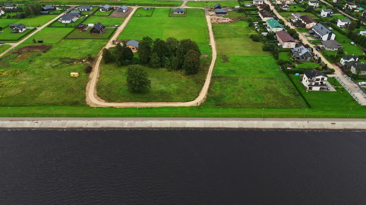 Daugava River glides past a green loop and waterfront homes as the promenade traces the shoreline—captured in a drone panning shot of riverside planning and natural balance in Ikšķile, Latvia