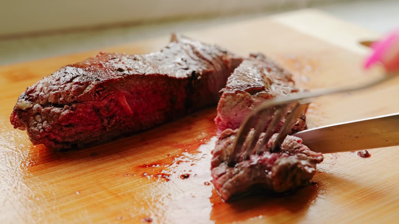 A freshly cooked steak is gently sliced on a wooden board with visible juice