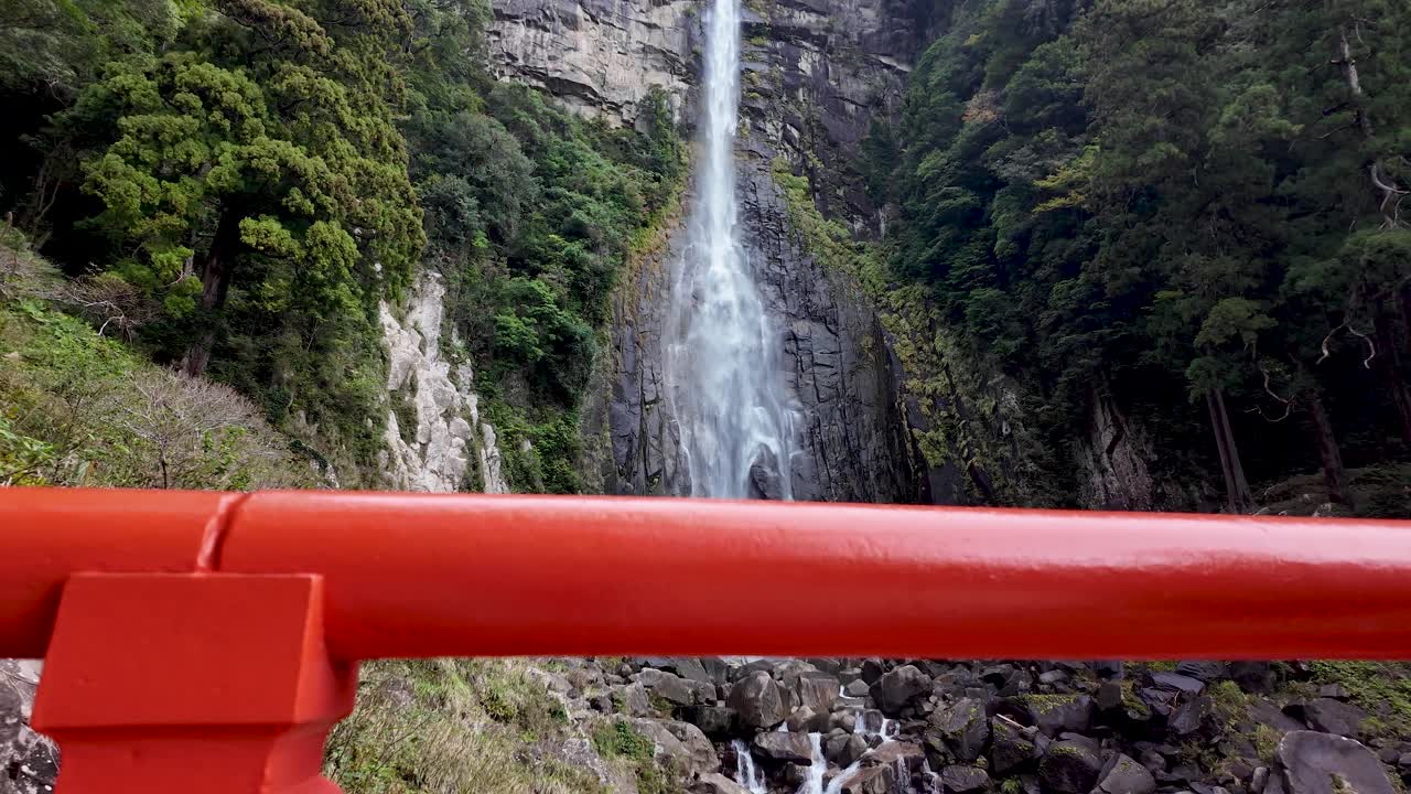 Low angle view of Nachi Falls, framed by a traditional red japanese shrine gate in Nachikatsuura, Japan. Push Forward Shot