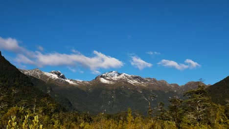 time lapse shot of flying clouds over mountain range during sunny day with blue sky - milford track in fiordland national park