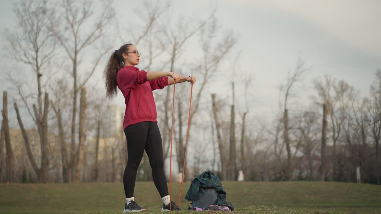 Female Exercise Outdoors, Lady Practicing Strength Exercises With Band Outside Chapel, Woman Engaging In Resistance Band Workout In Park With Historic Building Background In Morning Sunlight