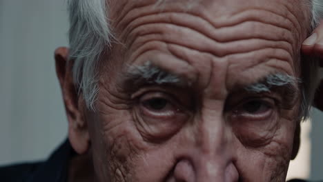 close-up of an elderly man's face, deep in thought or worry, with closed eyes and a hand on his temple