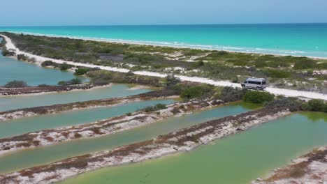 Aerial-of-camper-van-Driving-white-sand-road-with-Caribbean-ocean-and-salt-lake-view