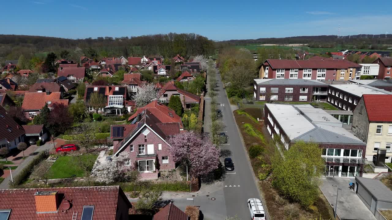 Idyllic housing area with Single Family houses and orange tile roofs. Car on tree-lined avenue on hill during sunny day in spring. Aerial forward wide shot.