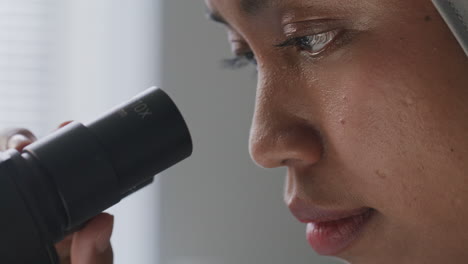 close up of female scientist in hijab looking through microscope