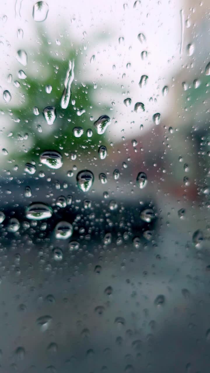 Calming vertical shot of rain on a window. Blurred nature background, ideal for serene, atmospheric, or weather-themed projects
