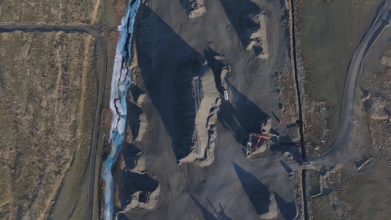 Aerial shot of heavy vehicle in dark grey quarry beside snowy river Iceland