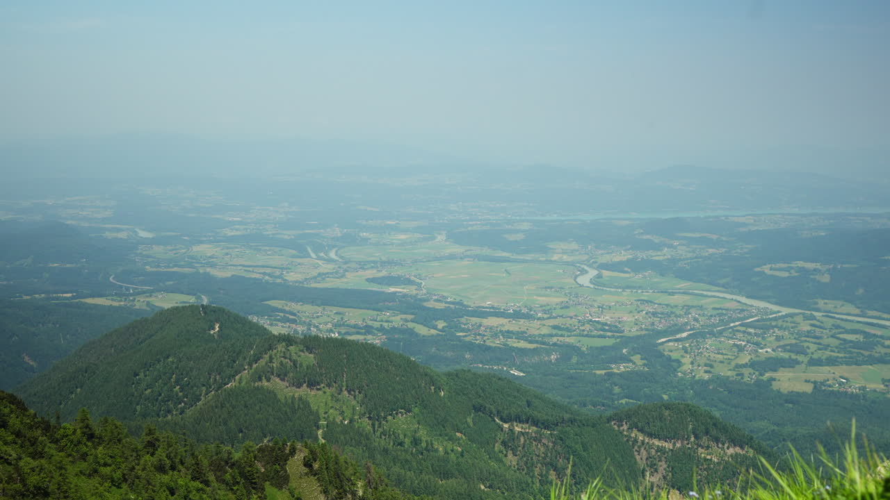 Scenic view from a Slovenian hilltop looking out toward Austria on a hot summer day. Hazy sky, green hills, and mountain layers fade into the distance, capturing peaceful nature and borderland beauty.