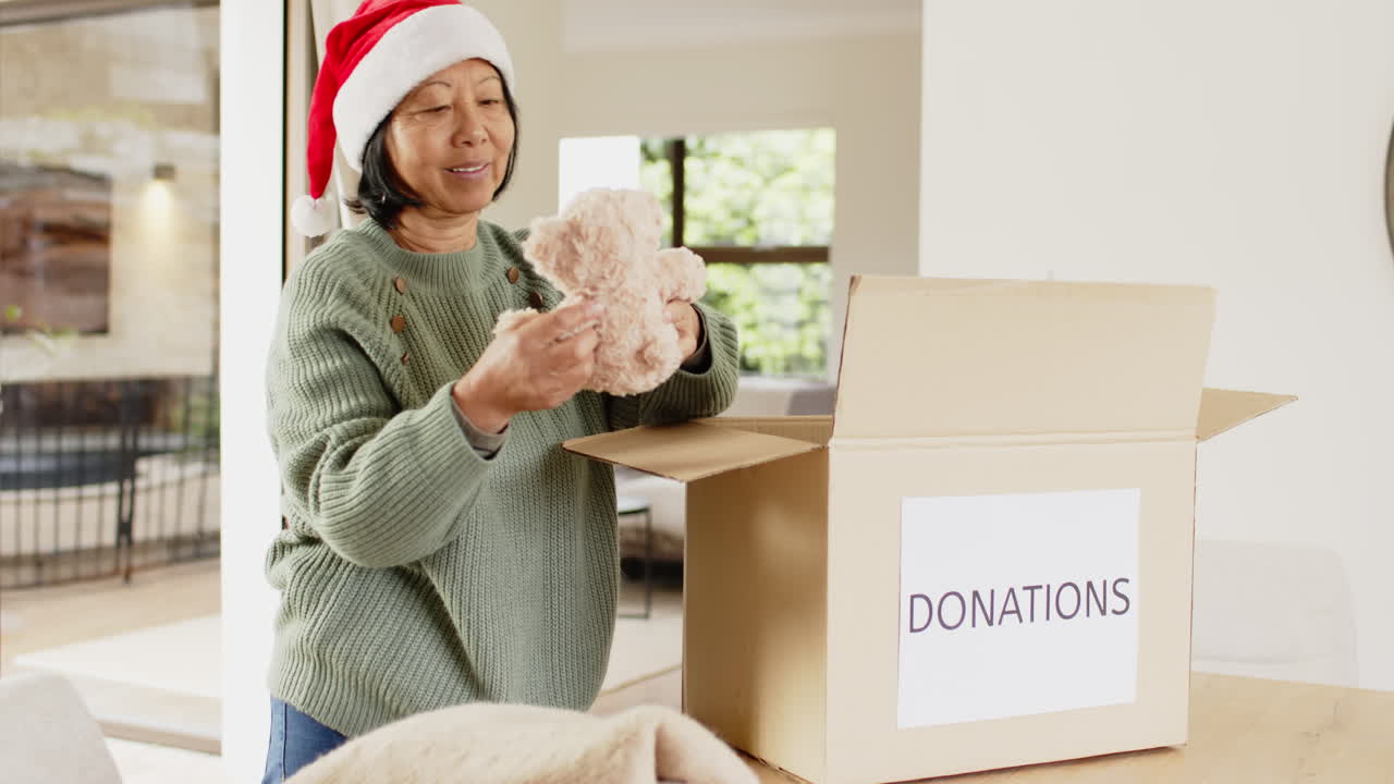 Smiling woman in Santa hat packing donation box at home during Christmas