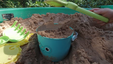 child patting a bucket full of sand with a spade, shot in a children's sand pit