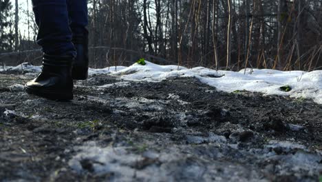 low angle close up footage of a person walking in a snow and dirt covered forest during a cloudy day. the camera shot is static and on the round while the person with black shoes steps in front of it.