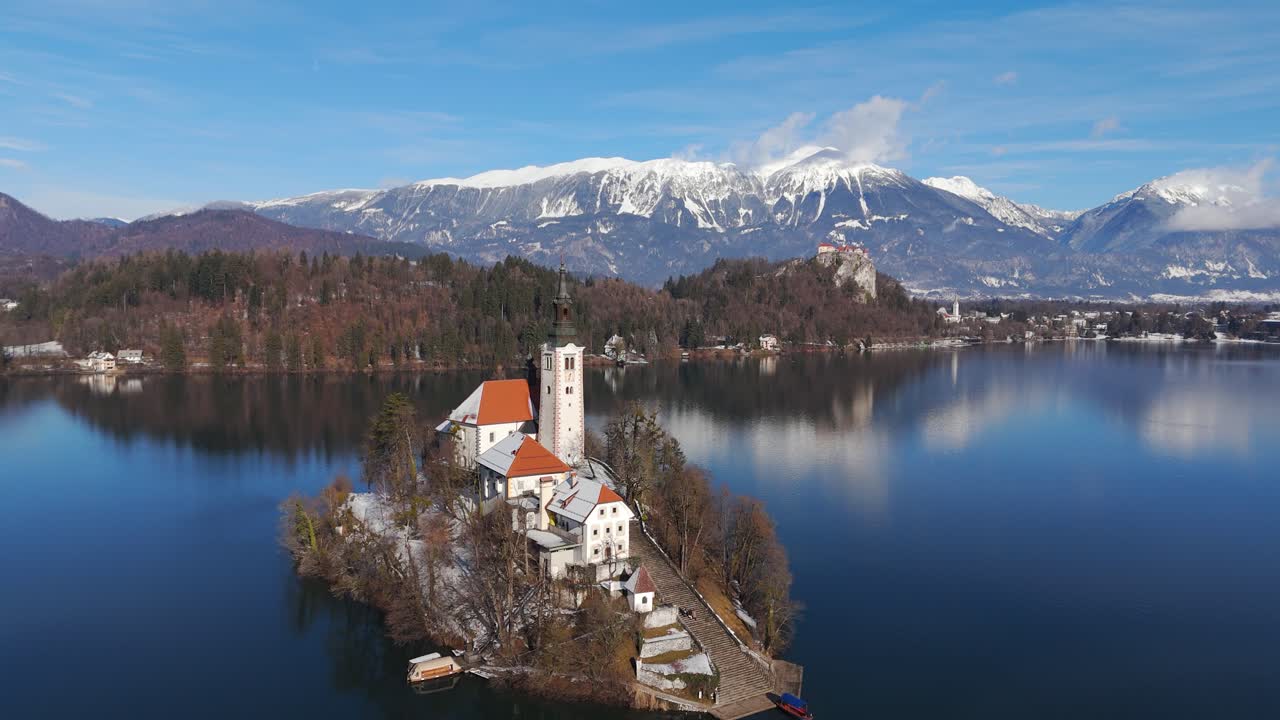 Vista aerea del lago di Bled in inverno, Slovenia, con la caratteristica chiesa sull'isola di Bled, acqua blu calma e montagne innevate sotto un cielo terso. Periodo invernale in Slovenia. Campo lungo all'indietro
