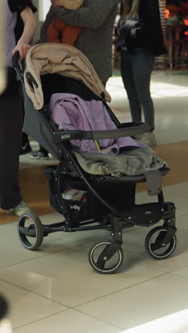 una escena de un centro comercial ocupado con diferentes personas que llevan varias ropas en el fondo. un cochecito de bebé aparece prominentemente, añadiendo al entorno dinámico