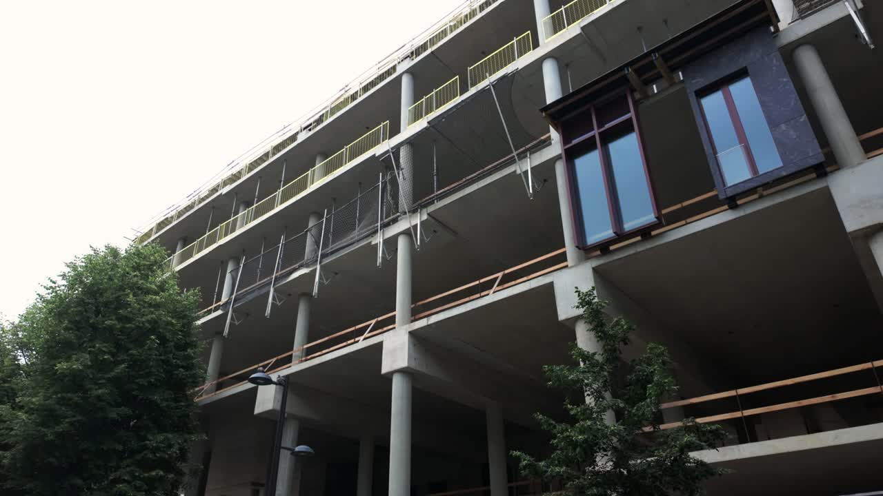 A modern multi-story concrete building under construction, showcasing exposed framework, columns, and an urban development setting in progress
