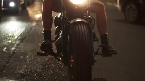 Front-view-of-a-bearded-motorcyclist-drives-a-bike-in-the-city-with-bright-headlight-at-night