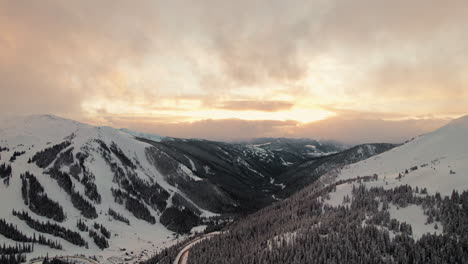 drone aerial footage flying over rocky mountains alpine valley slopes covered in pine trees during beautiful golden hour sunset in loveland pass, colorado usa