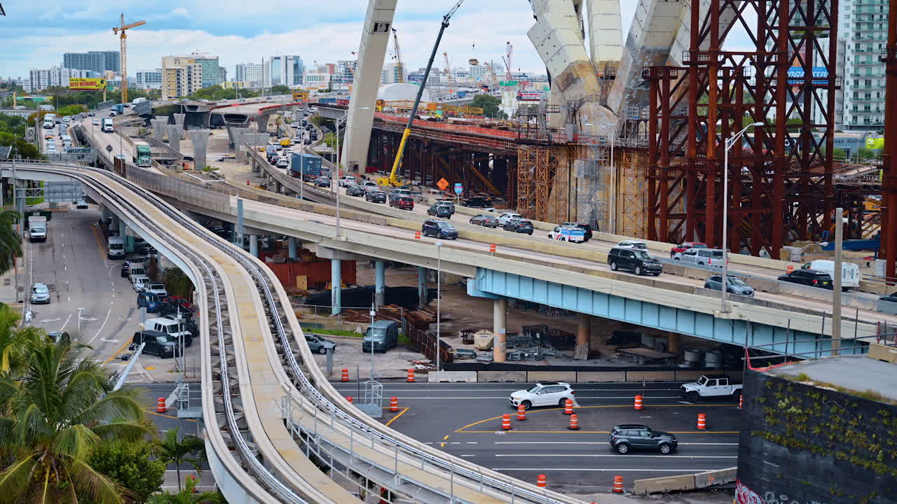 Miami, EE. UU., 16 de abril de 2026: Construcción del Puente Signature y tráfico en la autopista del centro de Miami. Proyecto de infraestructura a gran escala con grúas, estructuras de acero, vías del Metromover y coches.