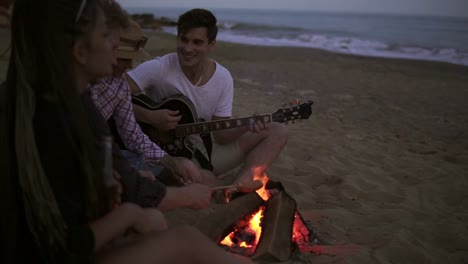 Picknick-Junger-Leute-Mit-Lagerfeuer-Am-Strand-Am-Abend.-Fröhliche-Freunde,-Die-Lieder-Singen-Und-Gitarre-Spielen.-Zeitlupe
