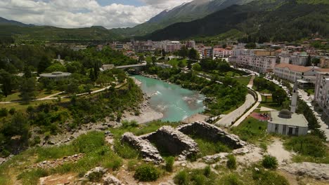 aerial-top-down-view-of-the-Permet-township,-located-around-the-Vjosa-river,-surrounded-by-mountains,-and-lush-greenery