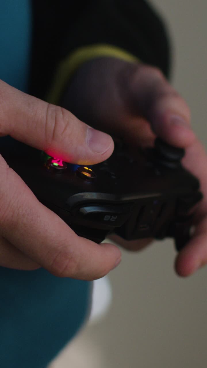 Video verticale: Primo piano laterale delle mani di un uomo in piedi che gioca con un controller per videogiochi a casa