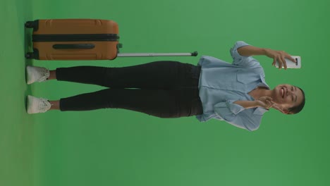 woman taking a selfie with suitcase in front of green screen