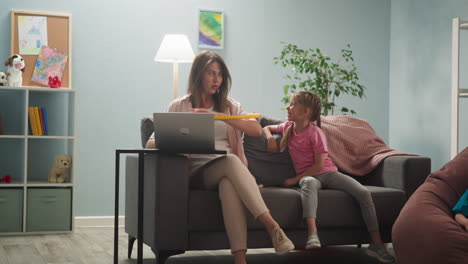 Girl-bothers-working-mother-with-hula-hoop-on-head-at-home