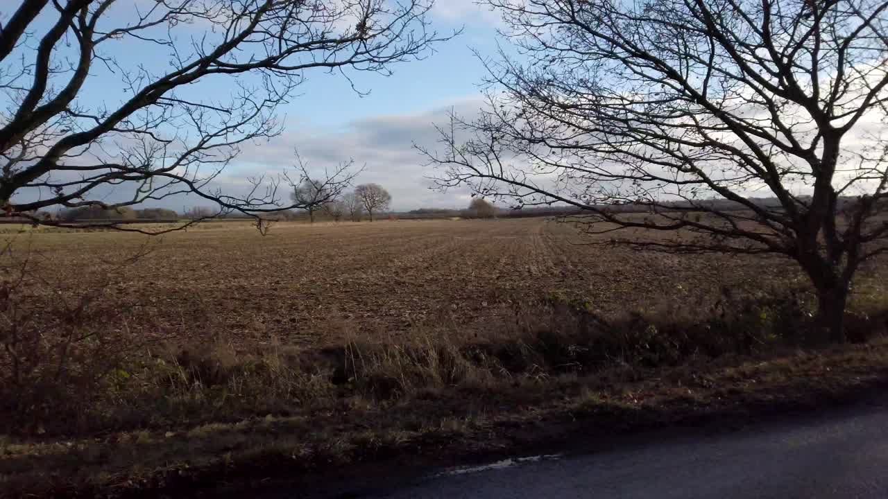 POV pan shot cycling past farmers fields in Winter in English Countryside