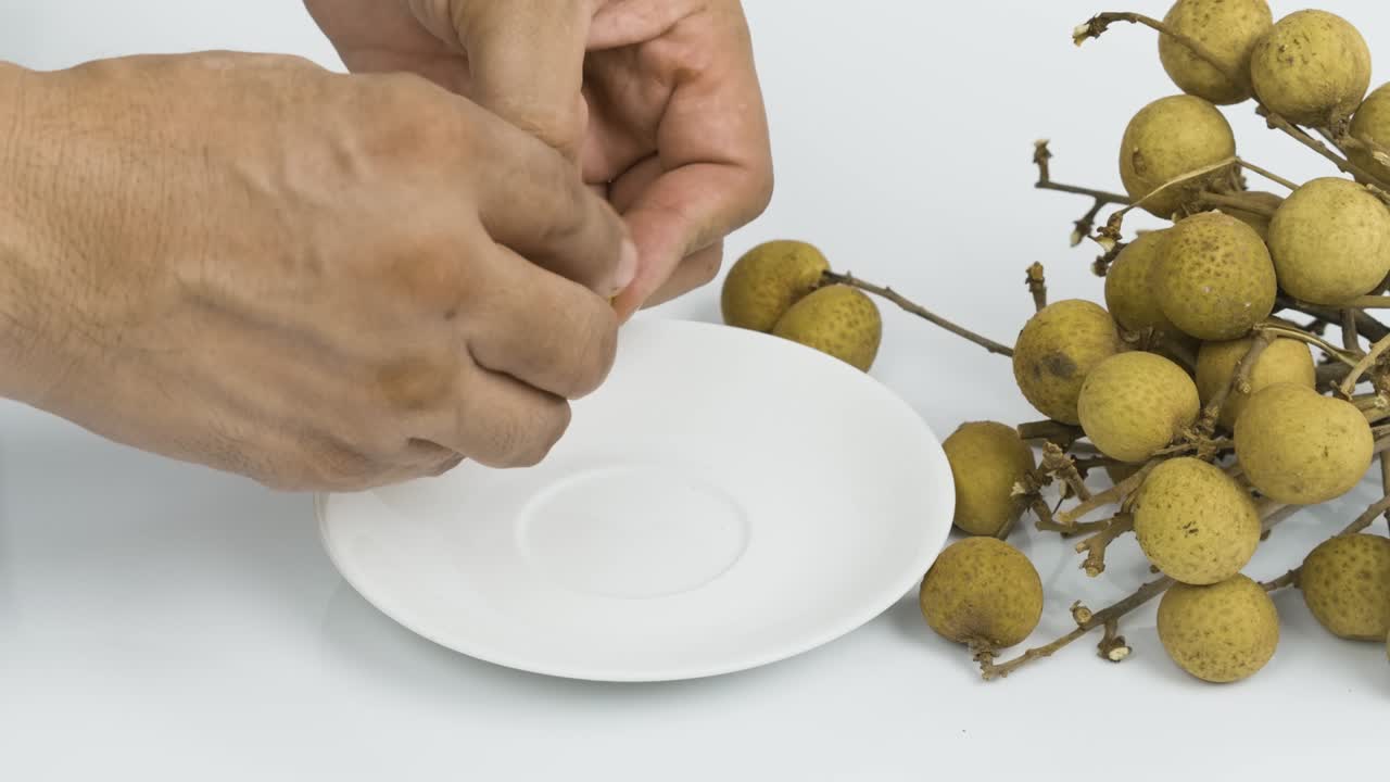 손으로 질을 벗기고 아시아 롱간 과일을  접시에 넣는다.