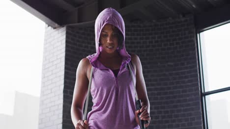 portrait of african american woman holding skipping rope wearing hoodie looking at camera in an empt