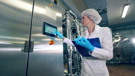 plant worker checks a machine, typing on display. female worker controls the quality of production equipment.