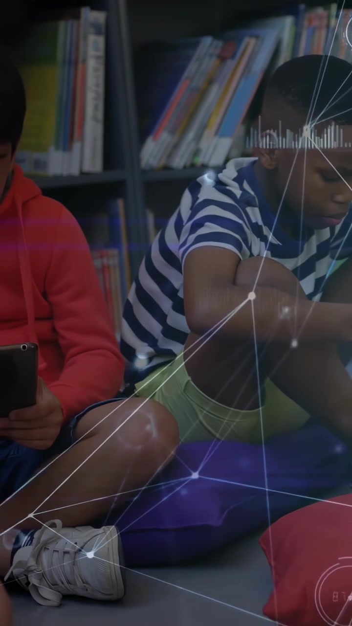 Vertical video: Child tapping tablet sparking HUD across library peer leaning forward both studying