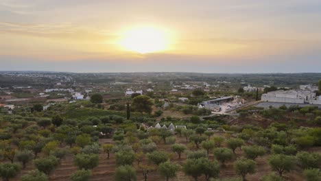 Vista-Aérea-Del-Paisaje-Sobre-Un-Pueblo-Rural-Con-Edificios-Blancos,-Rodeado-De-Olivos,-En-El-Campo-Italiano,-Al-Atardecer