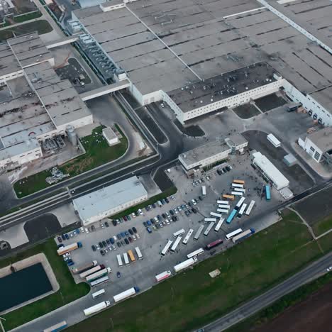 Factory on field near the road. Large production plant with car parking nearby. Cars and trucks moving on industrial territory.