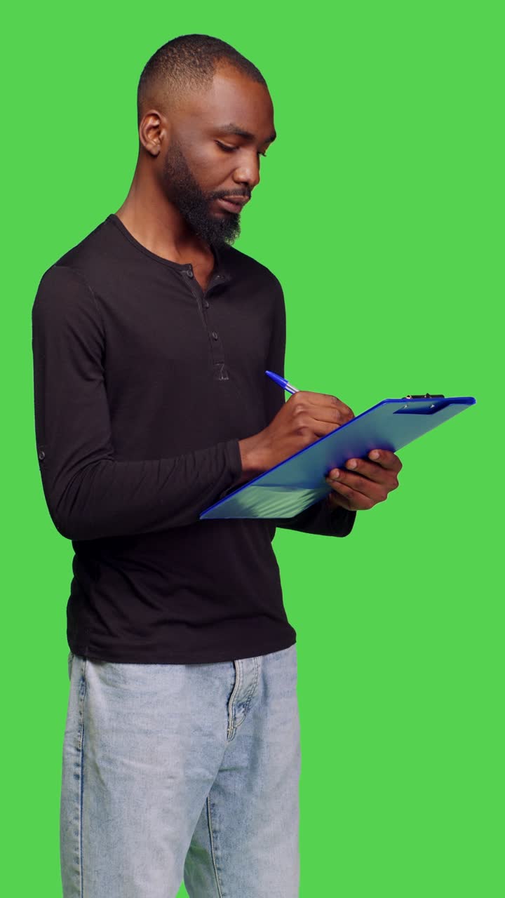 Vertical video: Side view of casual person taking notes on papers over greenscreen
