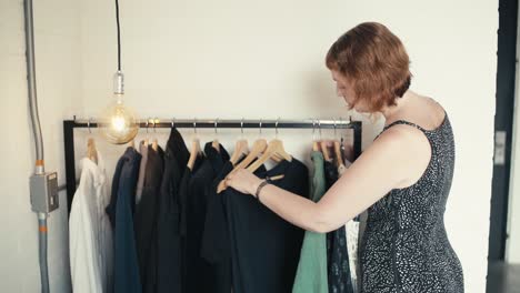 simple short red-haired woman choosing an outfit in the back room