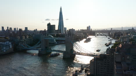 Boat-floating-under-Tower-Bridge.-Evening-forwards-fly-above-River-Thames.-View-against-sunshine.-London,-UK