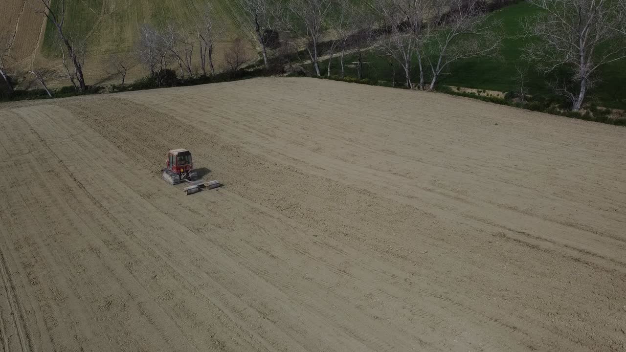 Red crawler tractor pull triple roll machine preparing the soil in agricultural farm, aerial view
