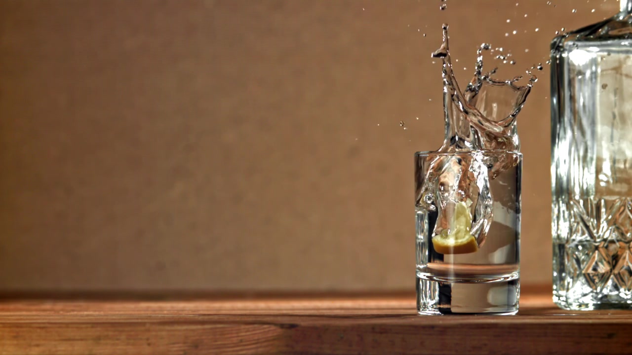 Fetta di limone che schizza in un bicchierino di vodka al rallentatore