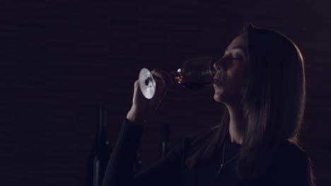 una dama está bebiendo lentamente disfrutando de su copa de vino tinto brasileño contra un fondo oscuro - cerrar