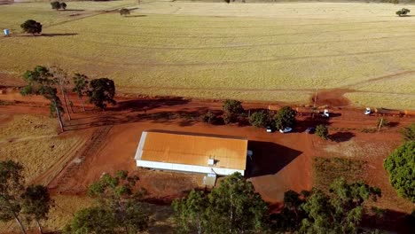 Rotating-Drone-View-of-Barn-building-Faon-Farm,-Trucks-driving-by-on-dirt-road