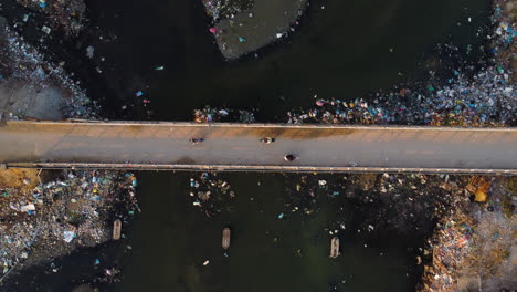 aerial top down, scooters driving on bridge over river polluted with plastic trash