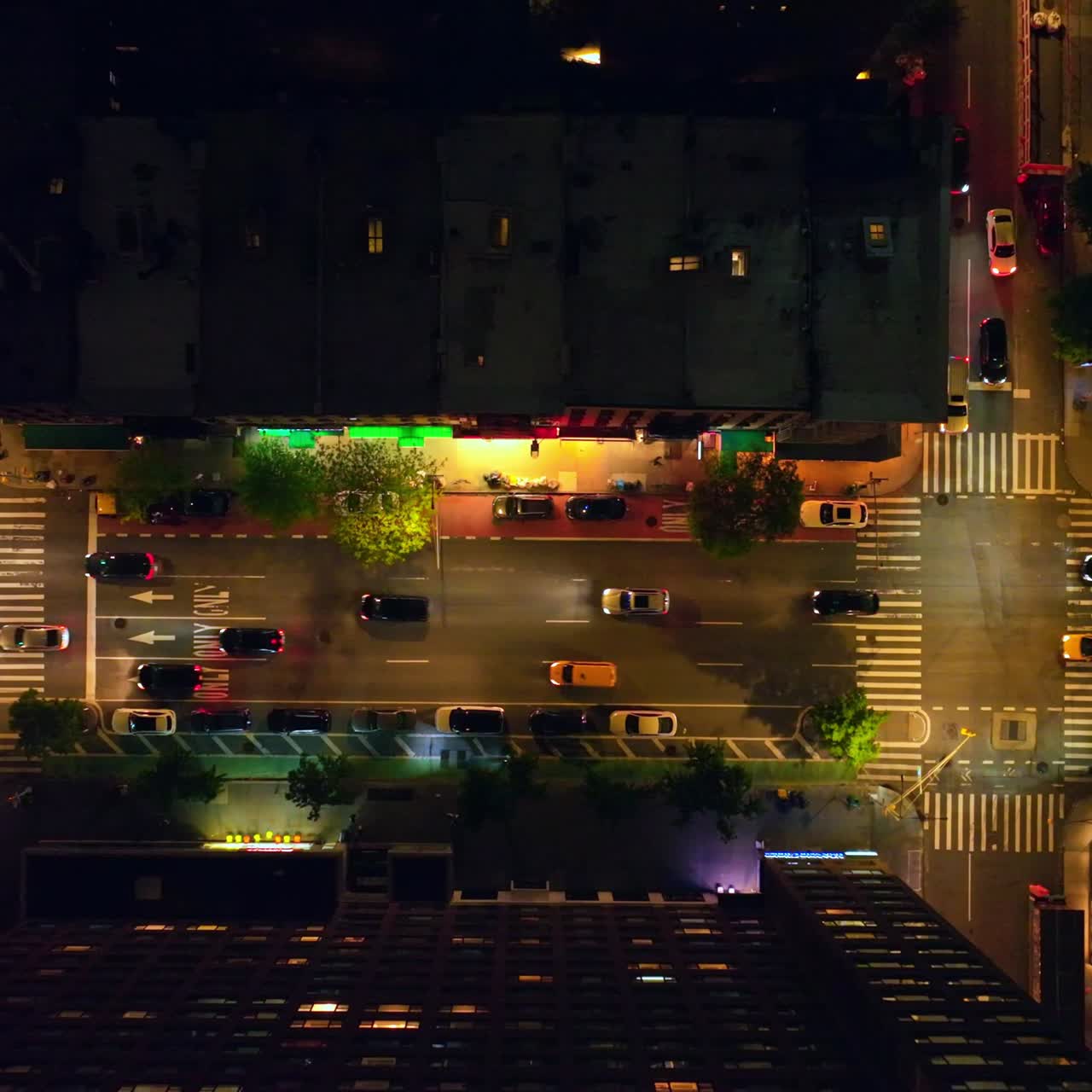 Beautifully lit streets of night New York. Lots of cars going along the roads and passing crossroads. Top view