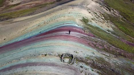 Aerial,-orbit,-drone-shot-around-a-man-hiking-the-Palcoyo-rainbow-mountain,-in-Valle-Rojo,-or-Red-Valley,-Andes-mountains,-sunny-day,-in-Peru,-South-America