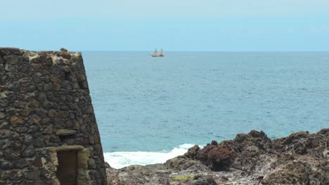 wooden sailboat near tenerife island in distance, rocky building in foreground