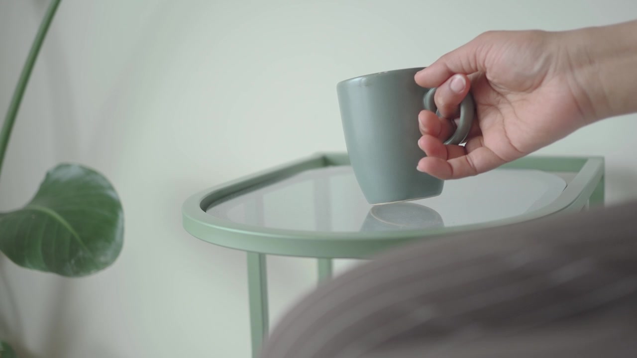 Close Up of Hand Picking Up a Green Mug from a Side Table