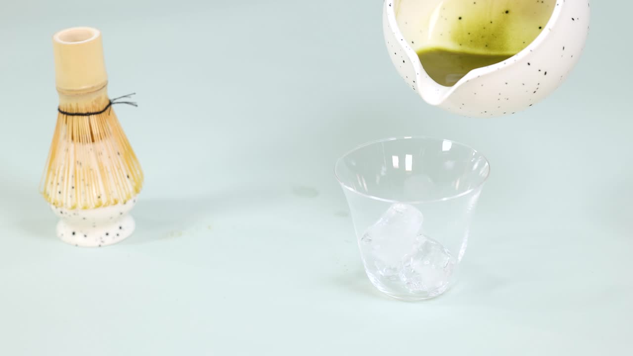 Hand pours vibrant matcha tea into iced glass, bright studio lighting, static camera shot